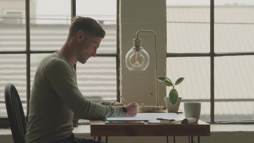 Man sitting at a table smiles while writing