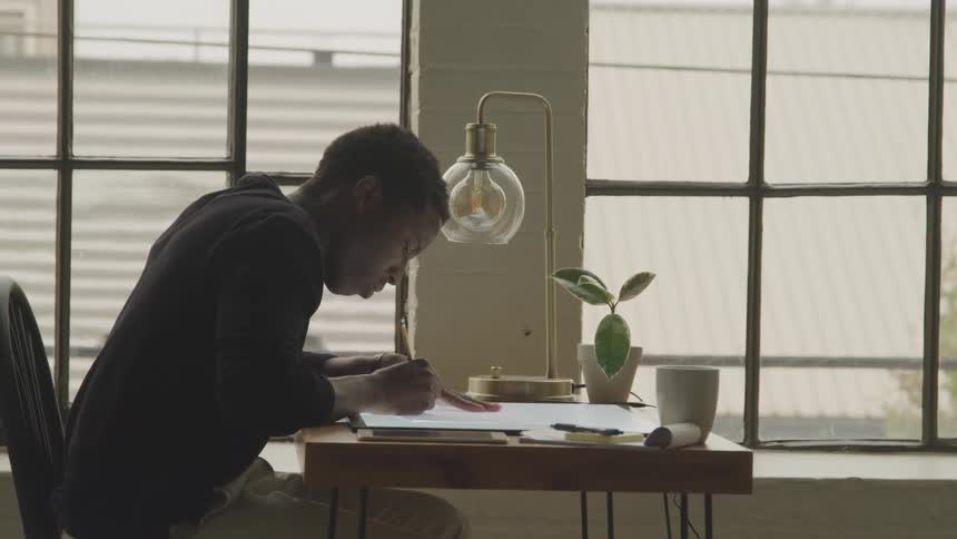 Man considers what he is drawing before putting pencil to paper at the table