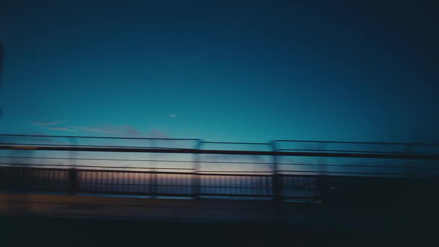 The sun sets behind a fencelined bridge
