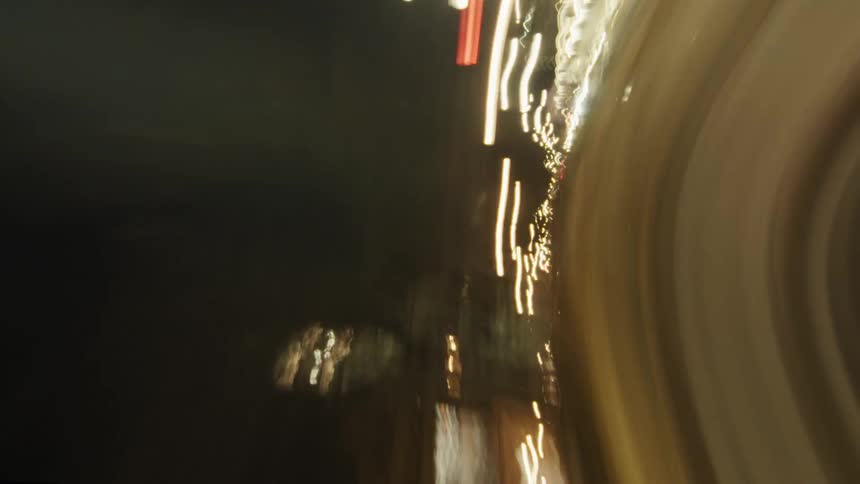 A violently spinning camera captures a chaotic blur of city lights streetlines and buildings in a distorted sideways rotation through an urban nightscape