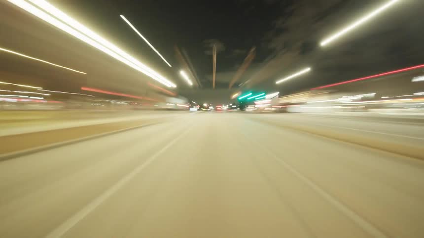 A highspeed reverse drive through a city street at night creates streaks of lights and motion blur under a cloudy sky