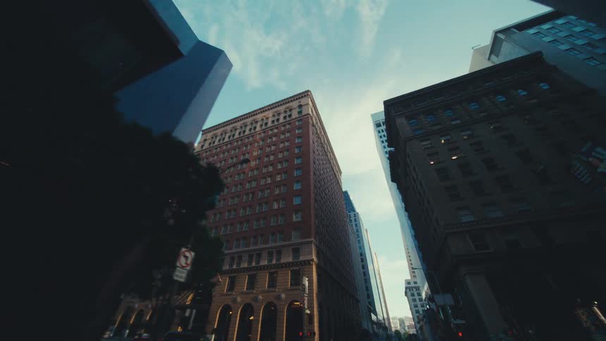 Looking up from street level tall buildings rise against clear blue sky at morning