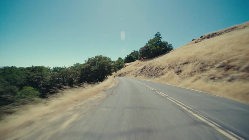 Road cuts through a grassy hill lined with trees