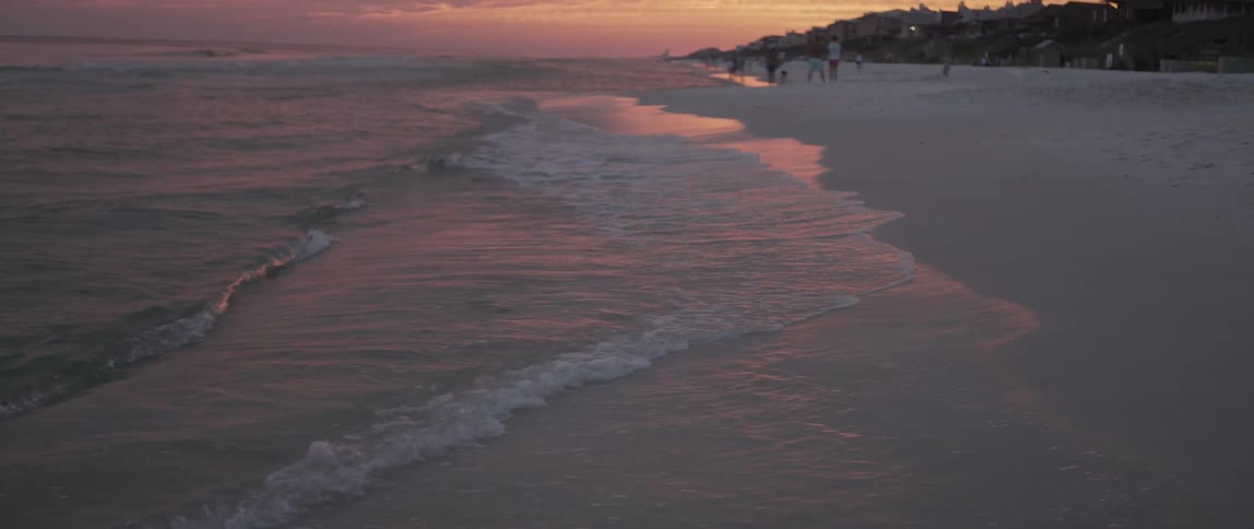 Waves coming in at shore on a beach at sunset with people walking around