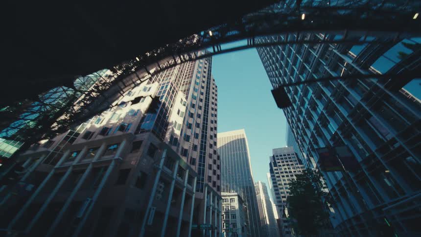 A low angle shot captures towering skyscrapers against a clear blue sky emphasizing the urban density and architectural scale