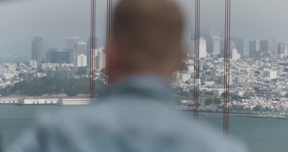 A man stands at a window and overlooks a river and a city