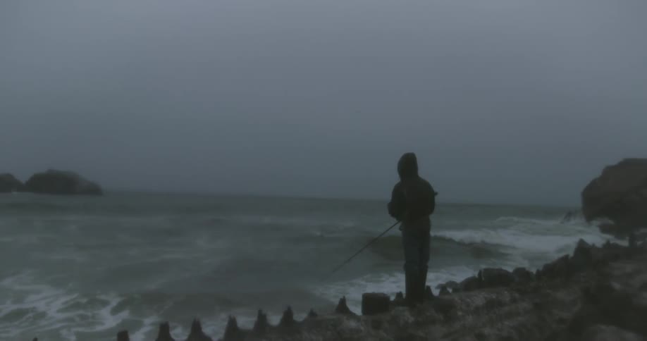 A man is fishing near a very rough coast