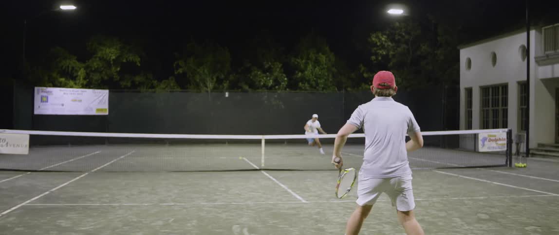 Two tennis players have a match at night