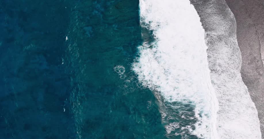 Aerial view captures ocean waves rolling toward the shore creating white wash patterns along the coastline