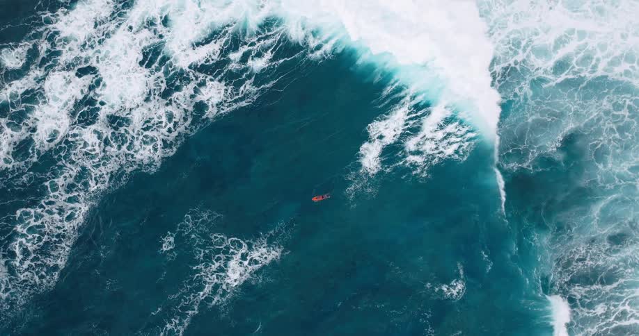 Aerial view of a man lying on his surfboard paddling as waves carry him