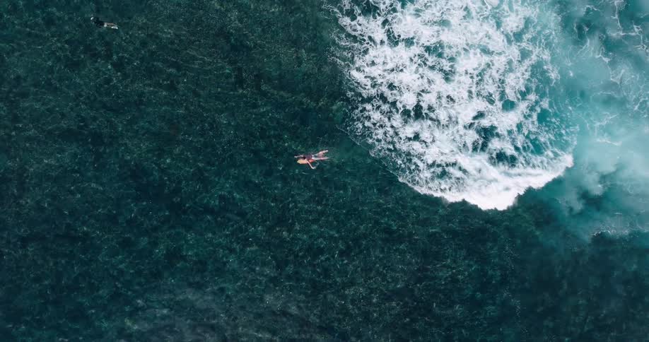 Birds eye view of surfer paddling away from crashing waves in the ocean