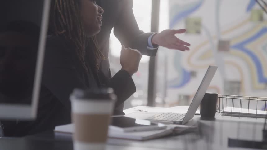 Coworkers refer to a laptop while collaborating at the office