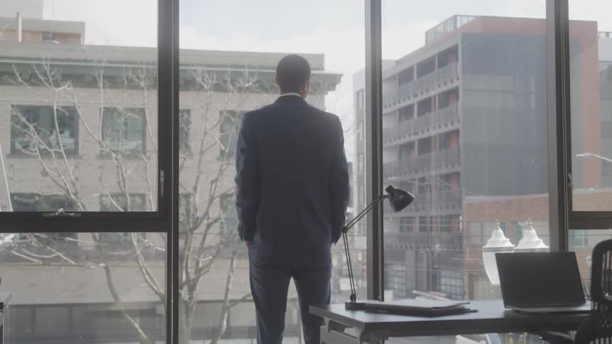 A man stands looking out the tall window