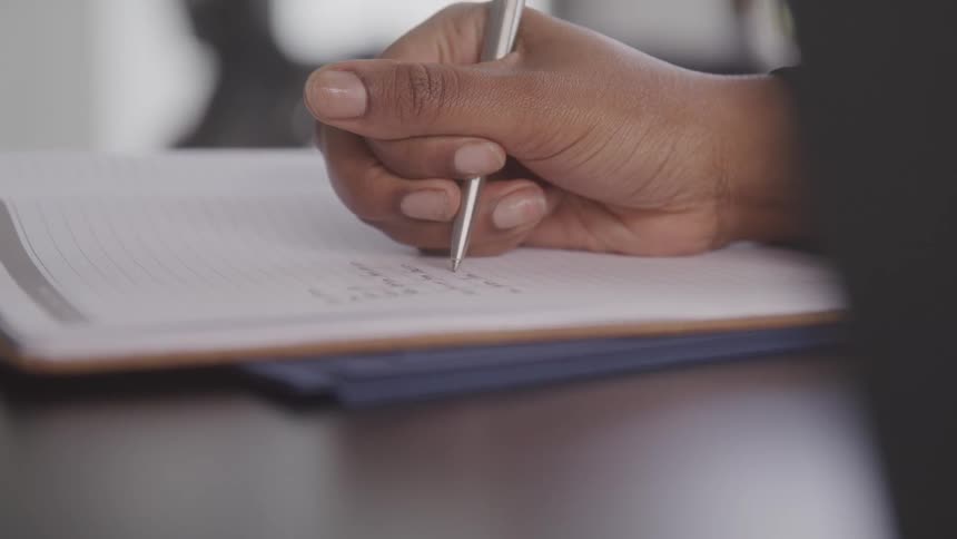 A hand is using a silver pen to write on a notepad