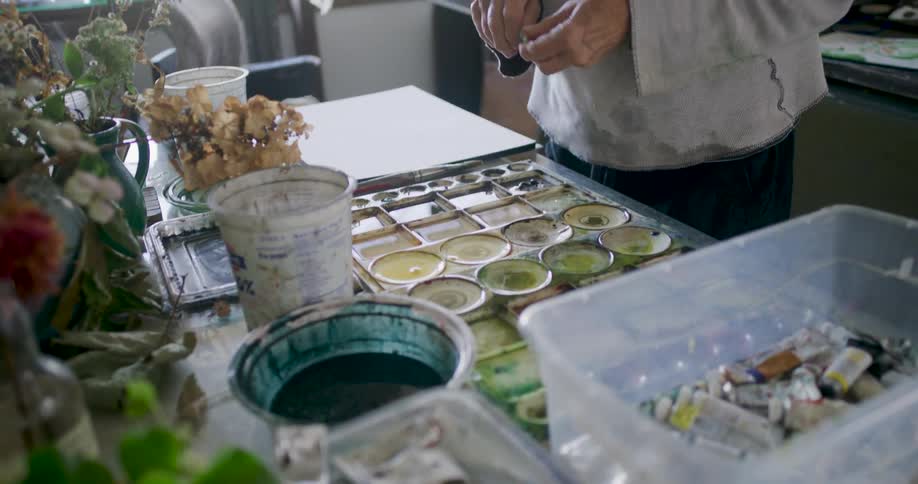 In an art studio an artist selects paint tubes and works with a palette preparing their materials