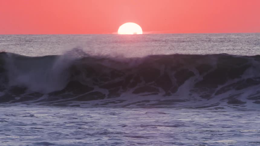 A half sun emerges from the horizon over a vast ocean casting a warm orange glow on the water and creating a serene sunset scene