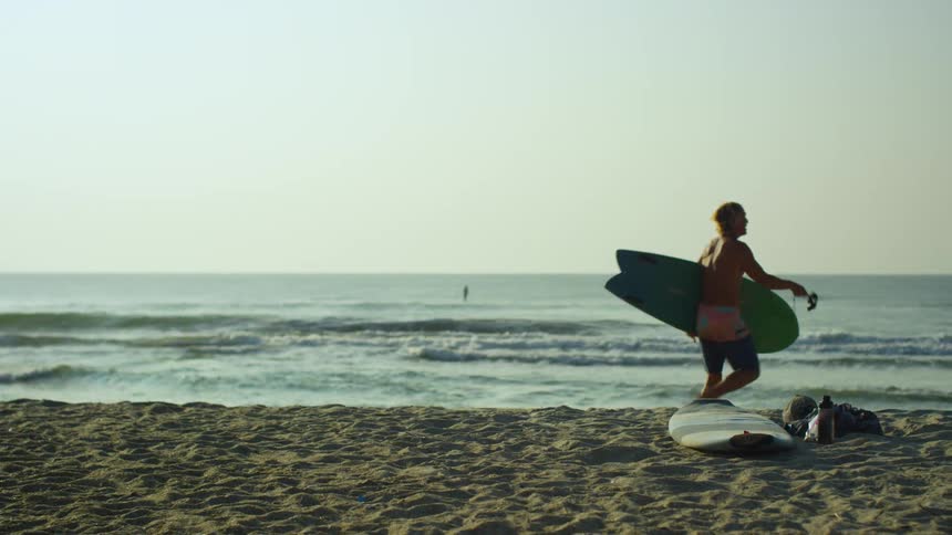 A man picks up his surfboard and heads in the ocean