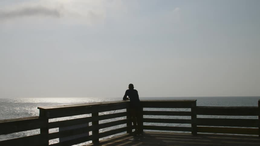 A man fishing in the ocean from a pier on a sunny day