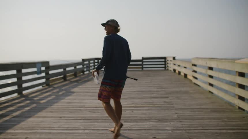 A man is walking on the boardwalk with his fishing pole