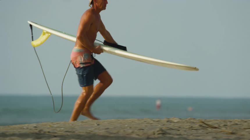 A man lays his surfboard on the sand