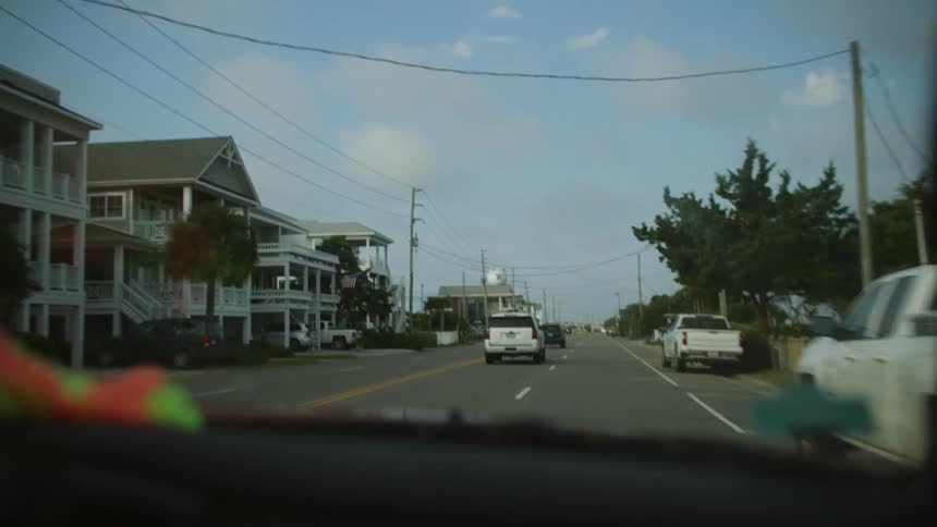 Vehicle travels along a road past large homes in a residential neighborhood on a cloudy day