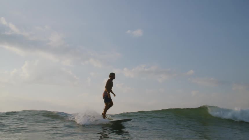 Surfer stands on his surfboard and rides a wave into shore