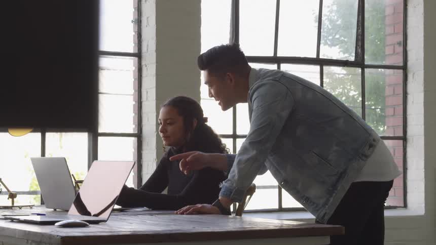 A man walks over to a woman typing on her laptop