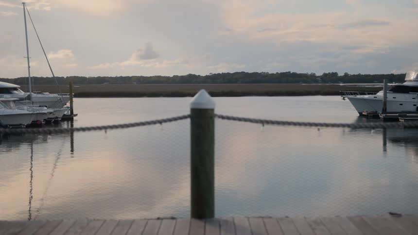 A peaceful view from a pier looking out at still waters and docked yachts under a quiet sky with only slight movement in the scene