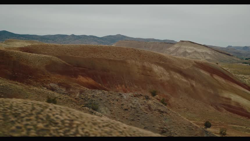 A vast arid landscape with rolling hills sparse vegetation and distant mountains under an overcast sky