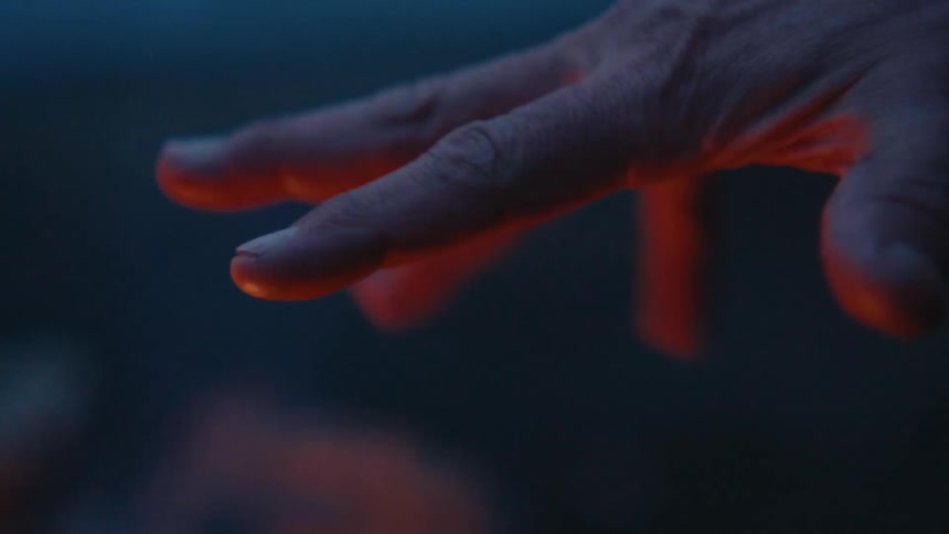 A man camping puts his hand over the fire