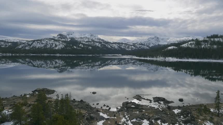 Snow-covered mountains and heavy clouds are reflected in a lake