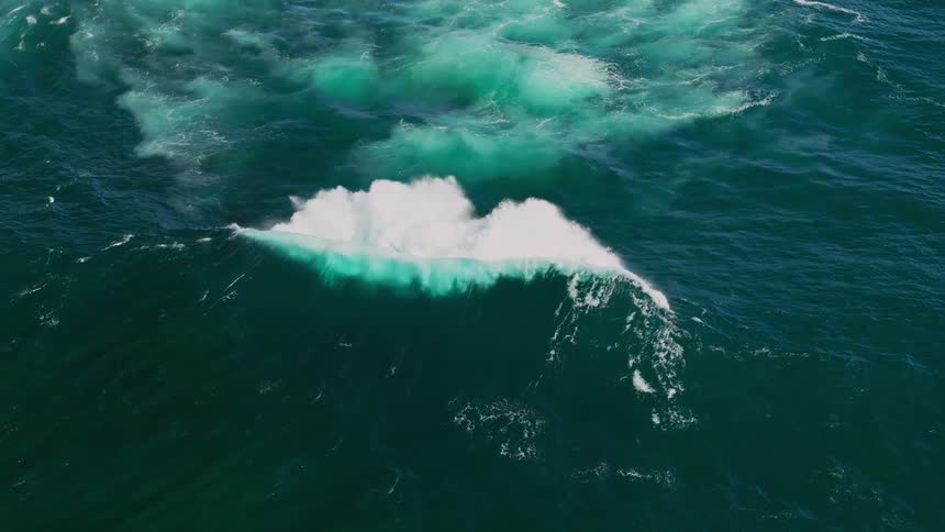 An aerial view of turbulent teal colored ocean water with a visible wake