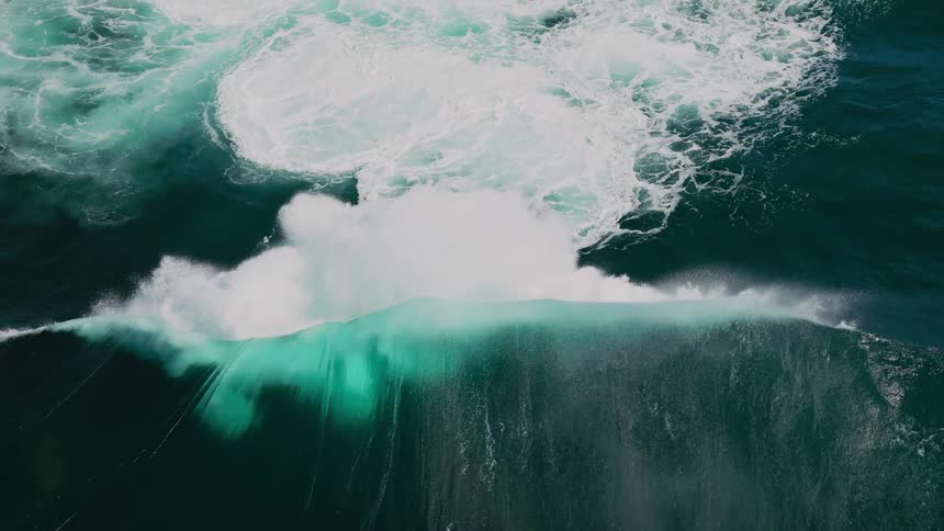 White foam froths and swirls energetically atop the deep bluegreen ocean as a wave rolls through