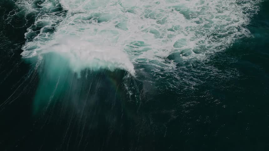White foam froths and swirls energetically atop the deep bluegreen ocean as a wave rolls through