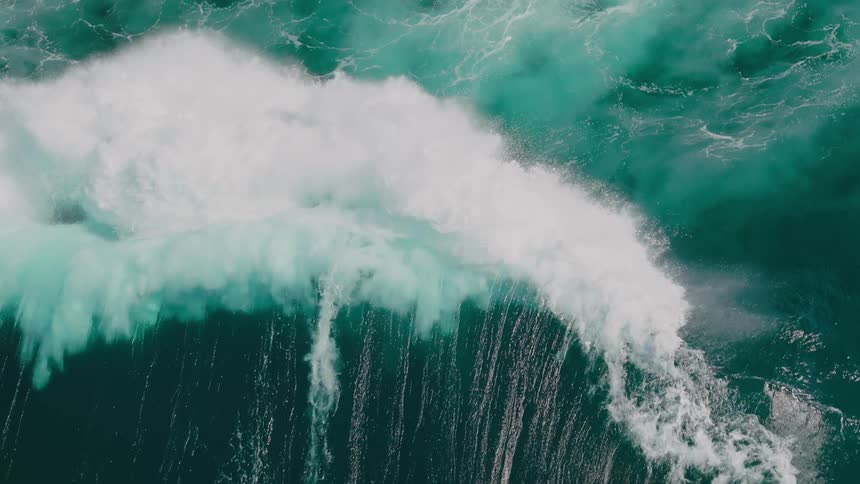 A wave crashing in the ocean with white foam contrasting against the deep blue green water