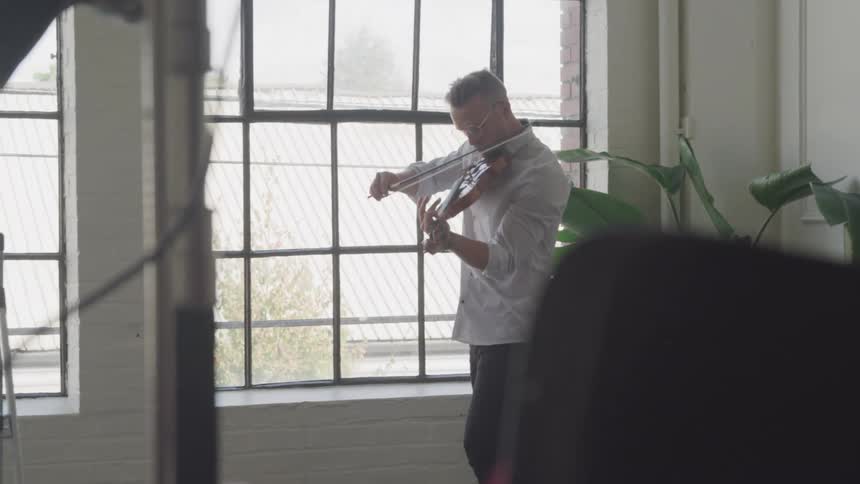 Man playing a violin next to a window in an apartment