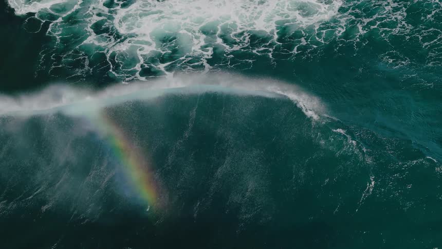 A large wave crashes in the ocean causing a rainbow