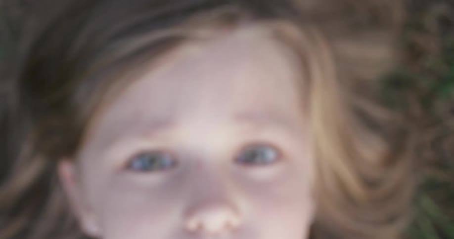 Little girls lays on ground outside looking towards the sky