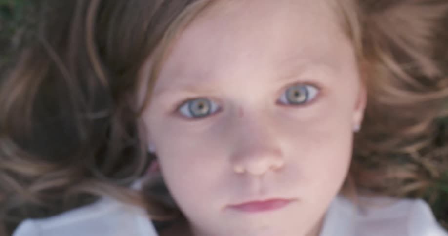 A child laying in the grass and looking at the camera