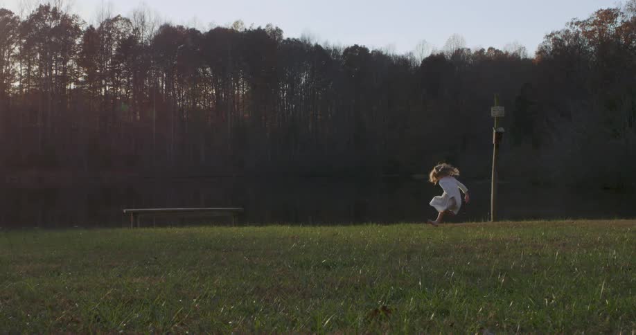 A girl runs and jumps on a grassy lawn next to a lake
