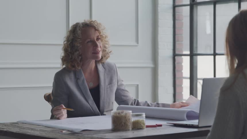A woman is holding a blueprint while talking at a meeting
