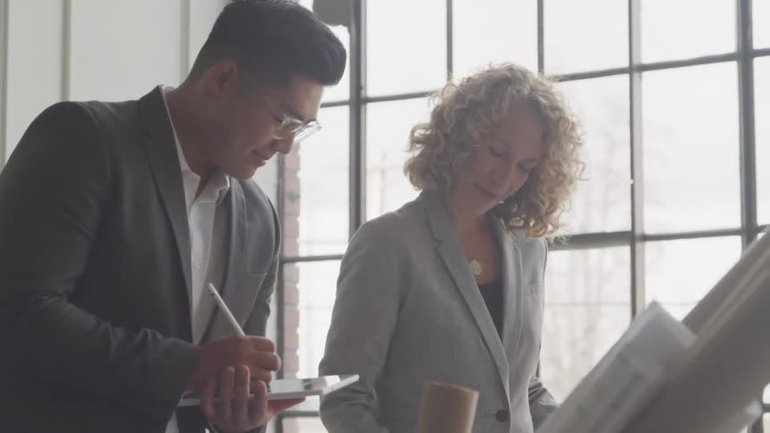 A man takes notes on his tablet while speaking with a woman in the office
