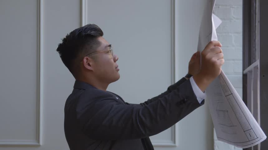 A man in a suit studies floor plans held aloft looking upwards as if visualizing the layout