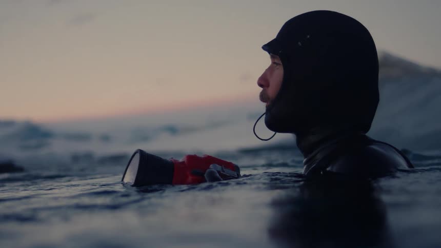 A scuba diver stands in the ocean holding a camera in front of him and looking around