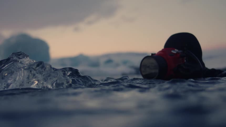 The man floats in the water photographing sea ice
