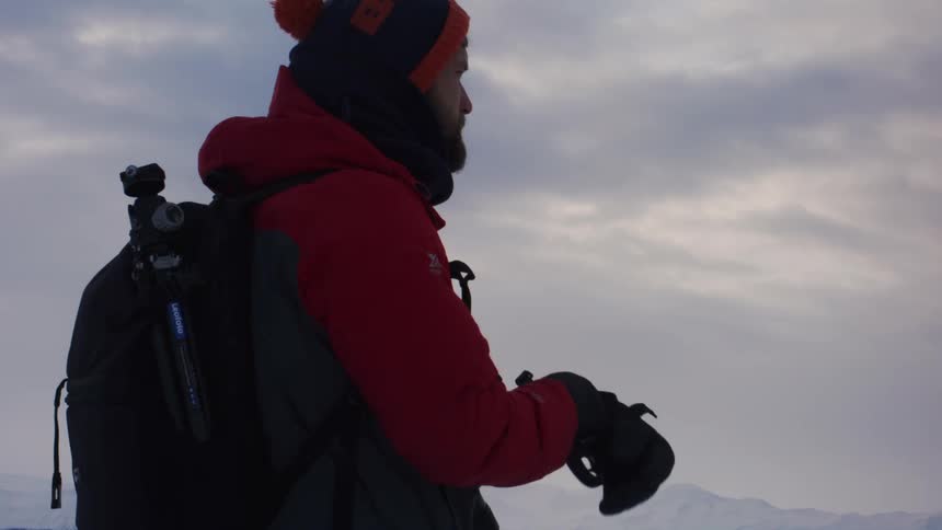 Male explorer stands outdoors and puts on his gloves while fog covers the mountainous landscape