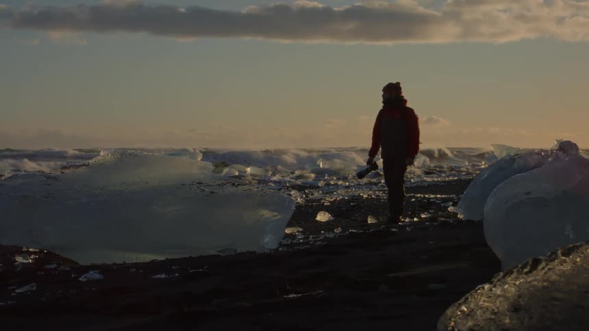 A man is carrying his camera past the sea ice