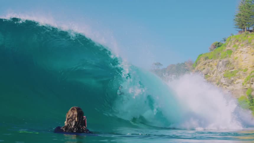 Person floating in the ocean takes video of a surfer riding through the barrel of a crashing wave on a sunny day