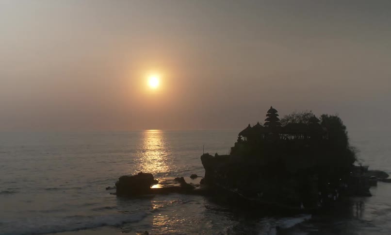 Tanah Lot temple in Bali silhouetted at golden hour in a timelapse overlooking the sea