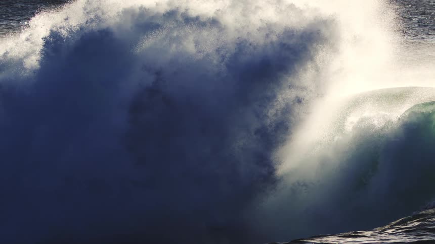 A huge ocean wave crashing and creating a mist cloud lit by sunshine